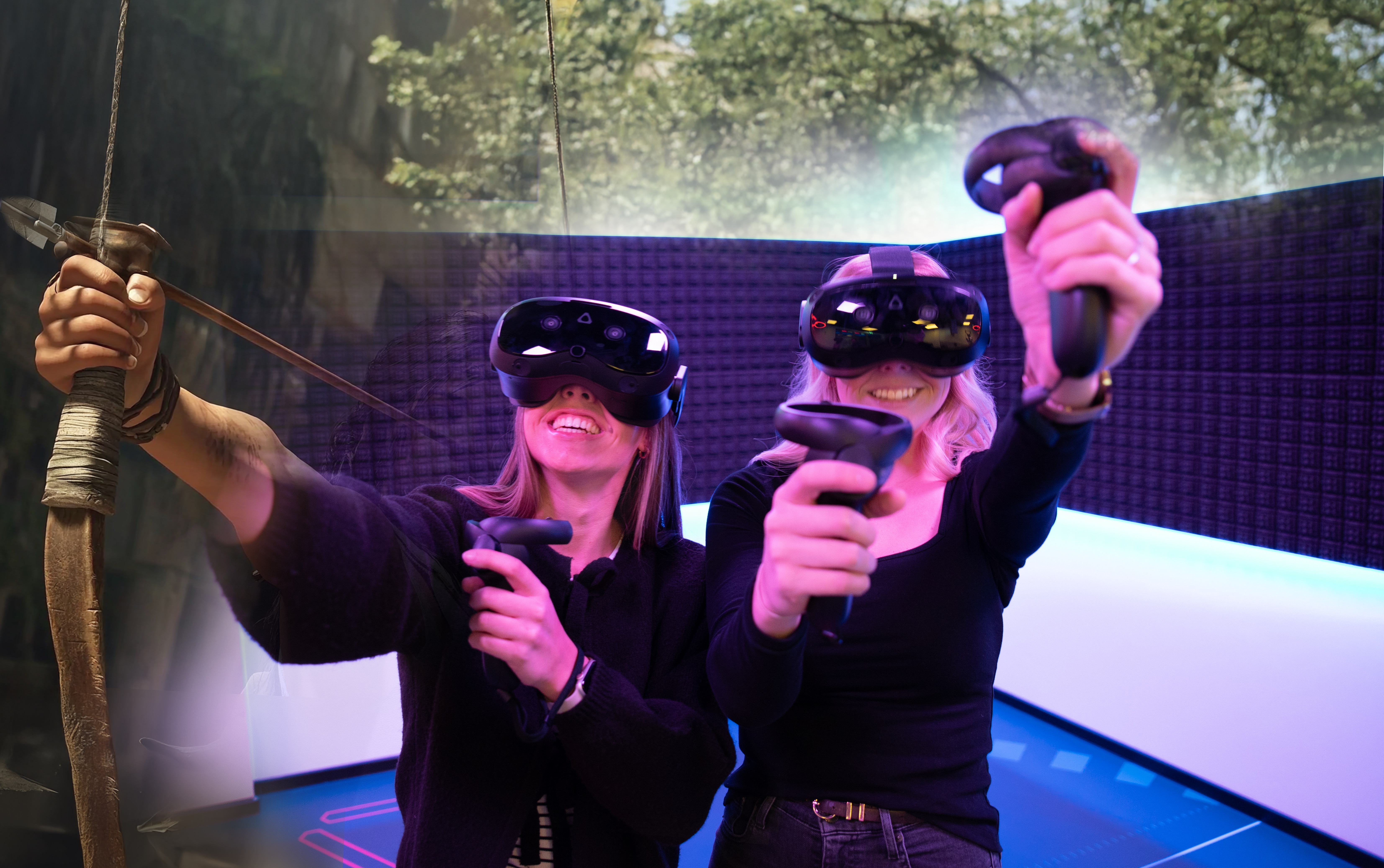 Zwei Personen mit VR Brillen und jeweils zwei Sticks in den Händen, welche sie in die Luft halten.