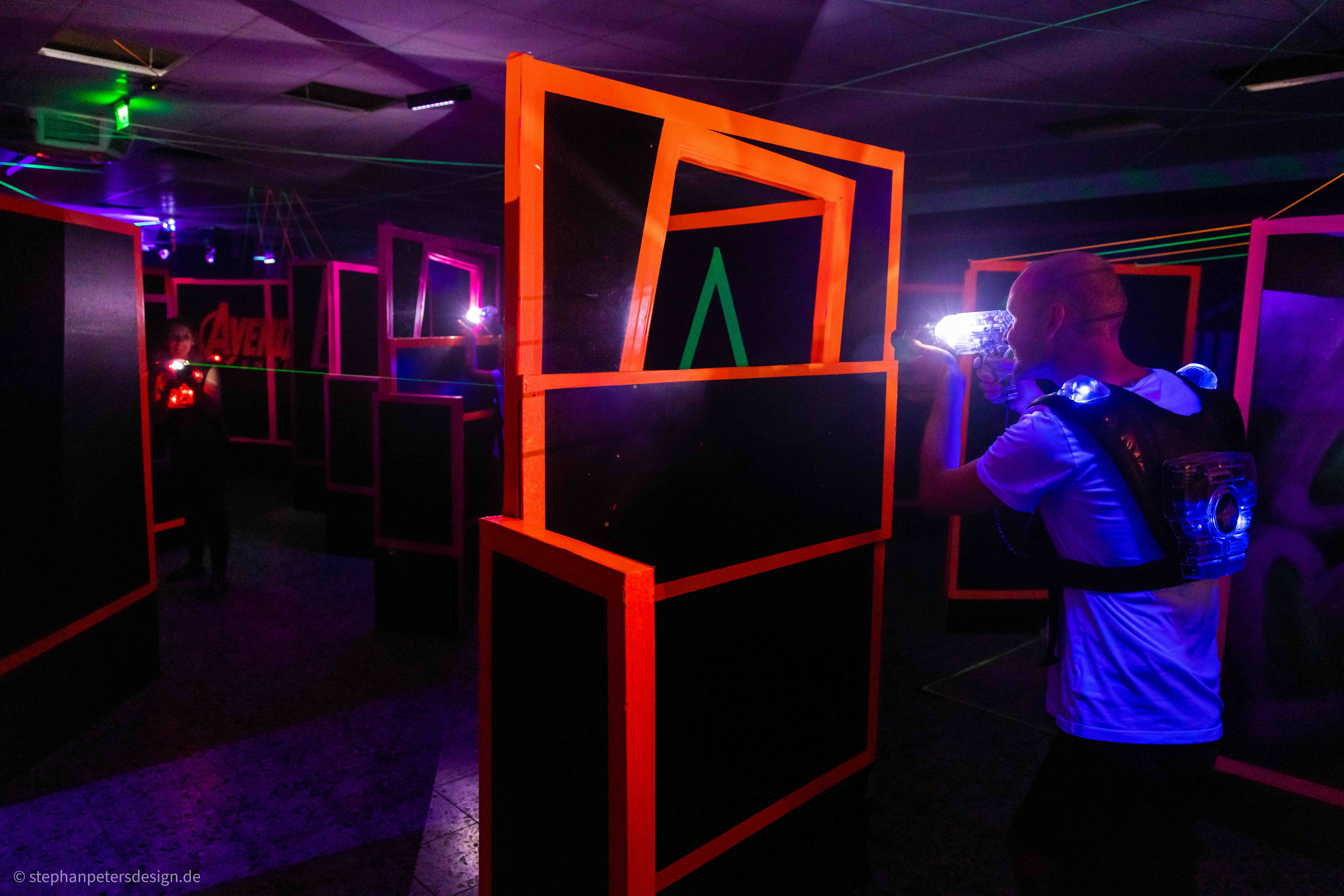 Eine Person in Schutzkleidung und mit Laserpistole hinter einer Schutzwand und versucht eine andere Person mit einem Laser zu treffen.