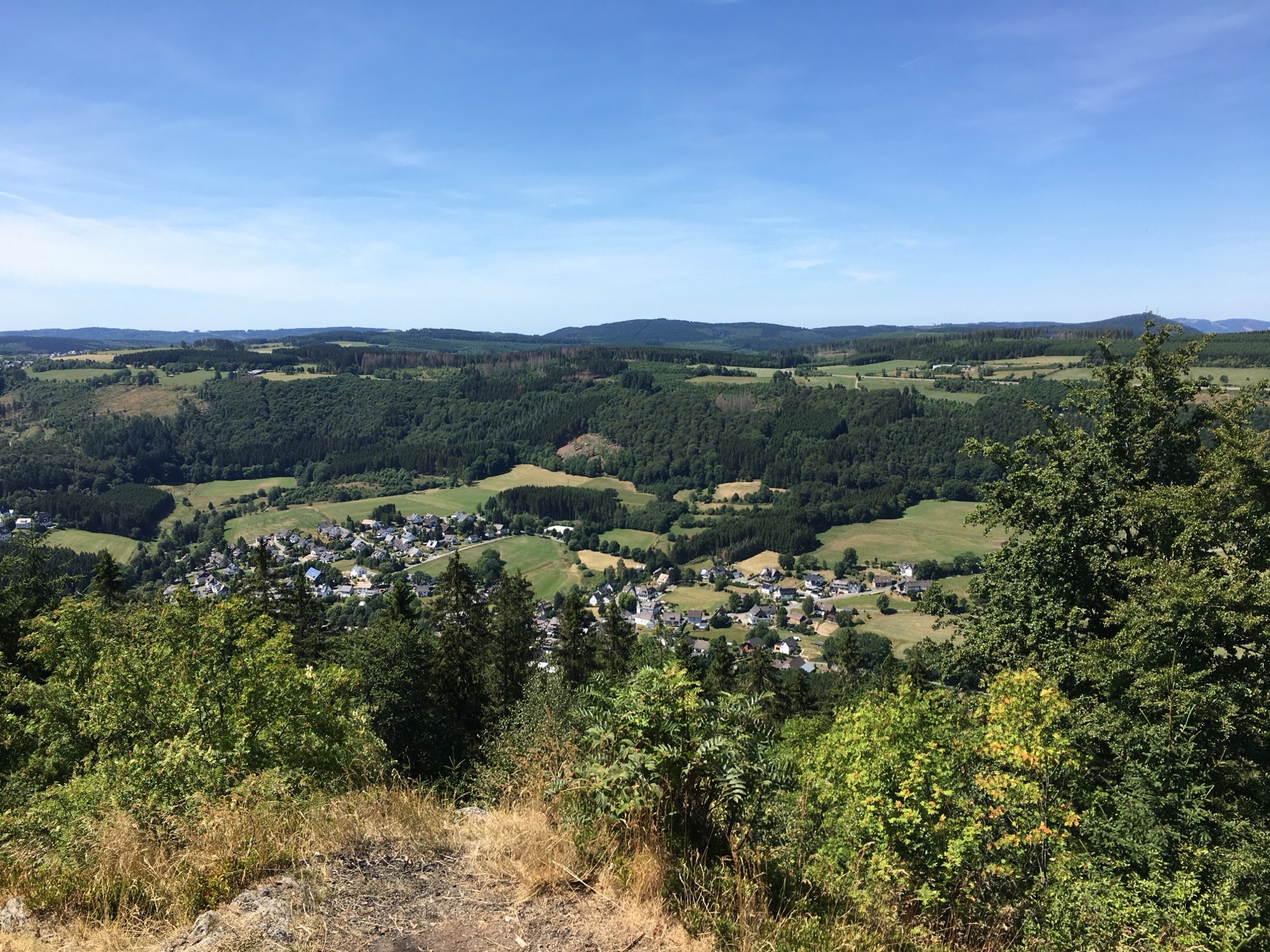 Ein Aussichtspunkt mit Blick ins Tal auf eine Ansammlung von Häusern umgeben von Wäldern und Wiesen. Ein Aussichtspunkt mit Blick ins Tal auf eine Ansammlung von Häusern umgeben von Wäldern und Wiesen.