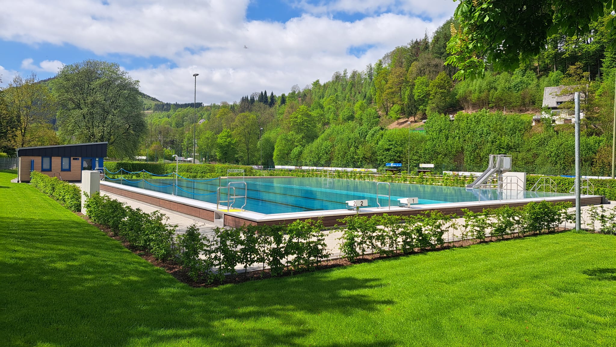 Ein Freibad mit großem Schwimmbecken umgeben von einer Liegewiese und Wald. Ein Freibad mit großem Schwimmbecken umgeben von einer Liegewiese und Wald.