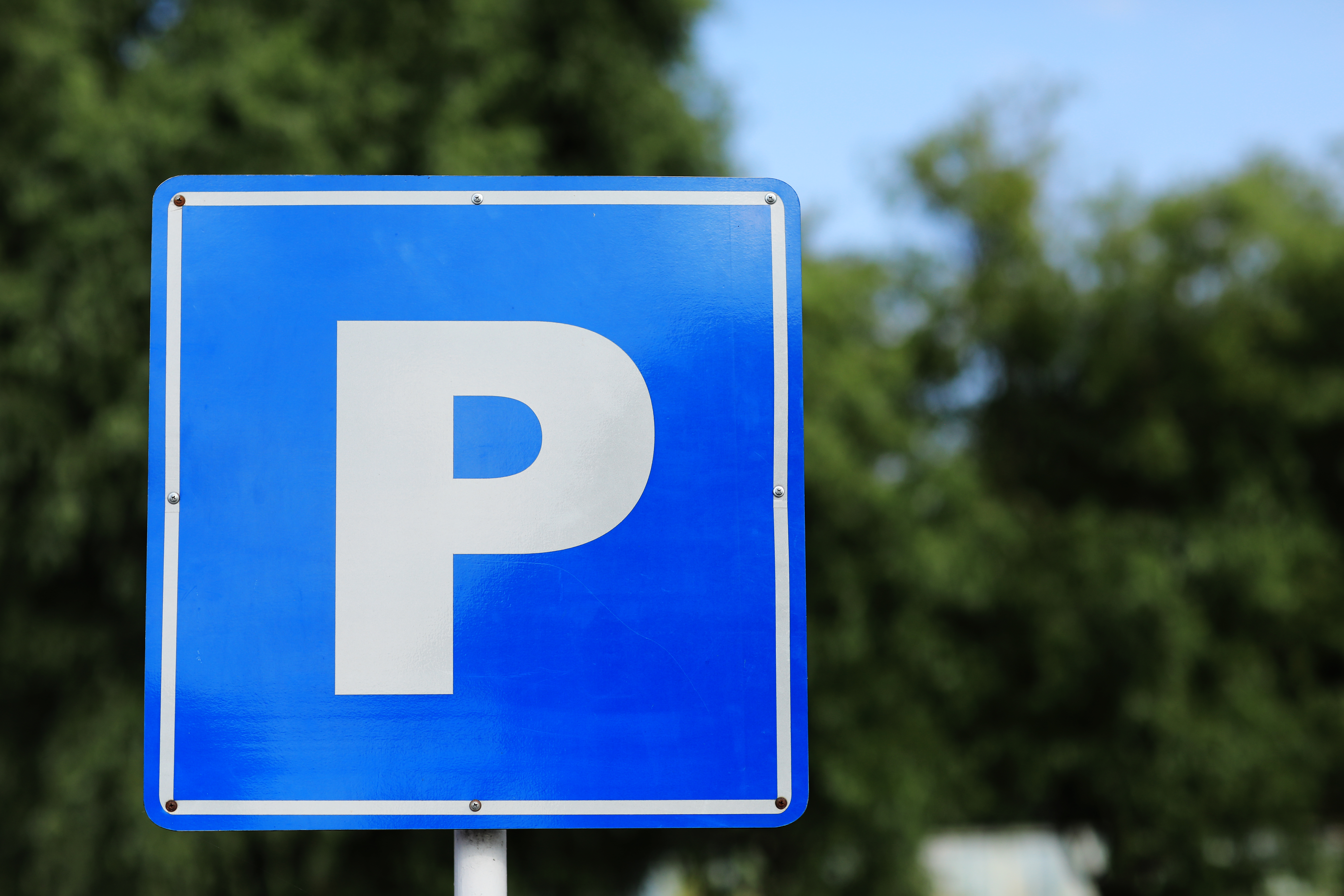Ein blaues Parkplatzschild mit einem weißen P vor Bäumen im Hintergrund. Dieses Bild dient als Symbolbild für Parkplätze.