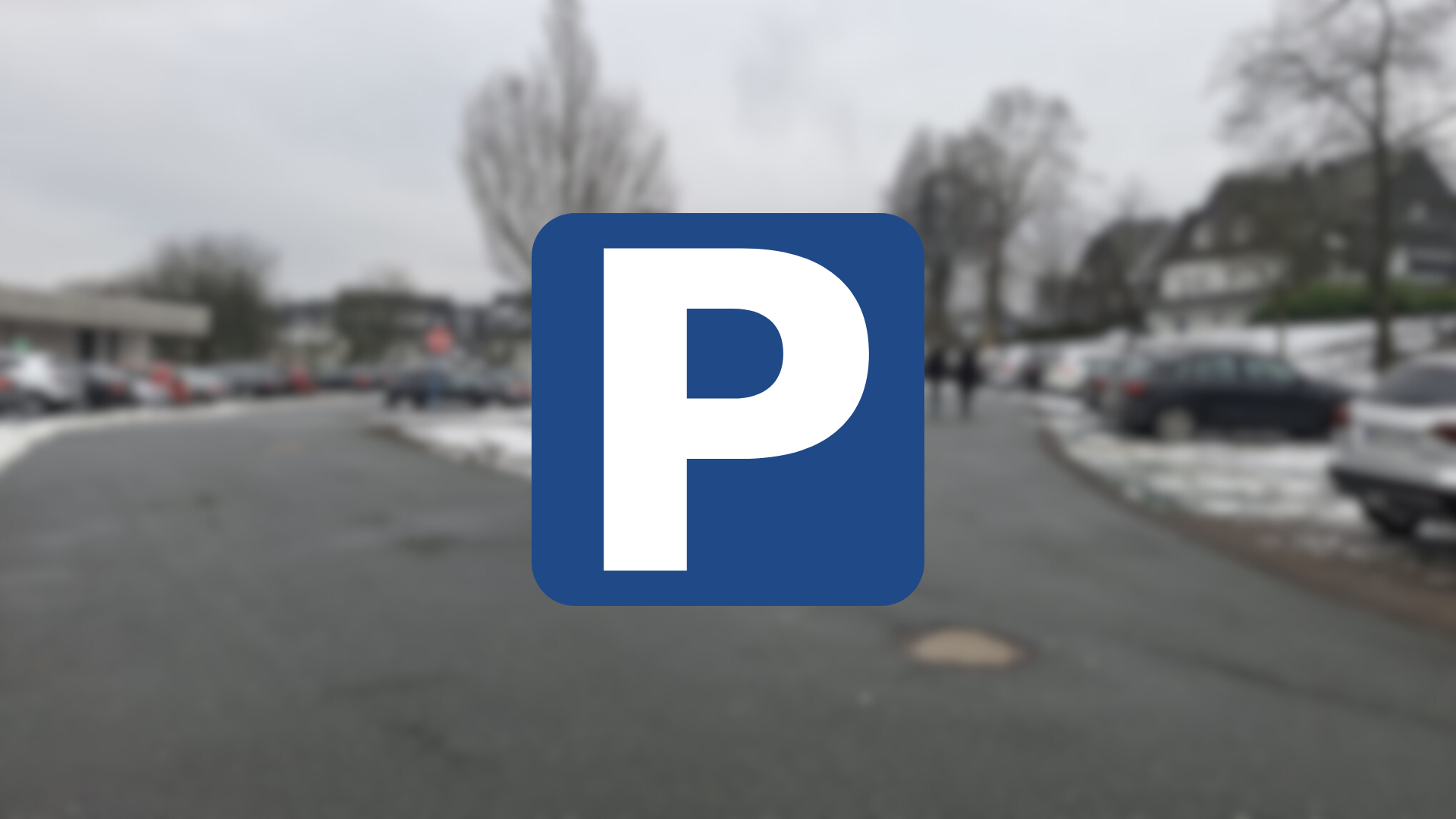 Ein verschwommenes Bild eines Parkplatzes mit einem Parkplatzschild mit weißem P auf blauem Grund im Vordergrund. Dieses Bild dient als Symbolbild für Parkplätze.