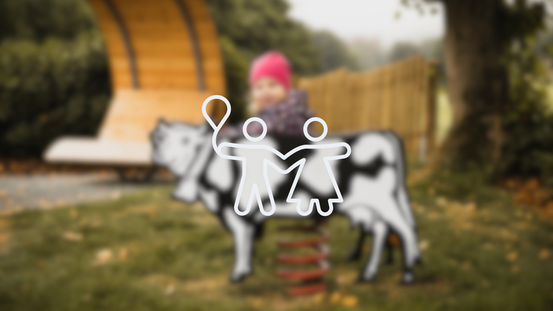 Ein verschwommenes Bild eines Kindes auf einem Wipptier mit der Zeichnung zweier Männchen, die sich an den Händen halten im Vordergrund. Dieses Bild dient als Symbolbild für Spielplätze.