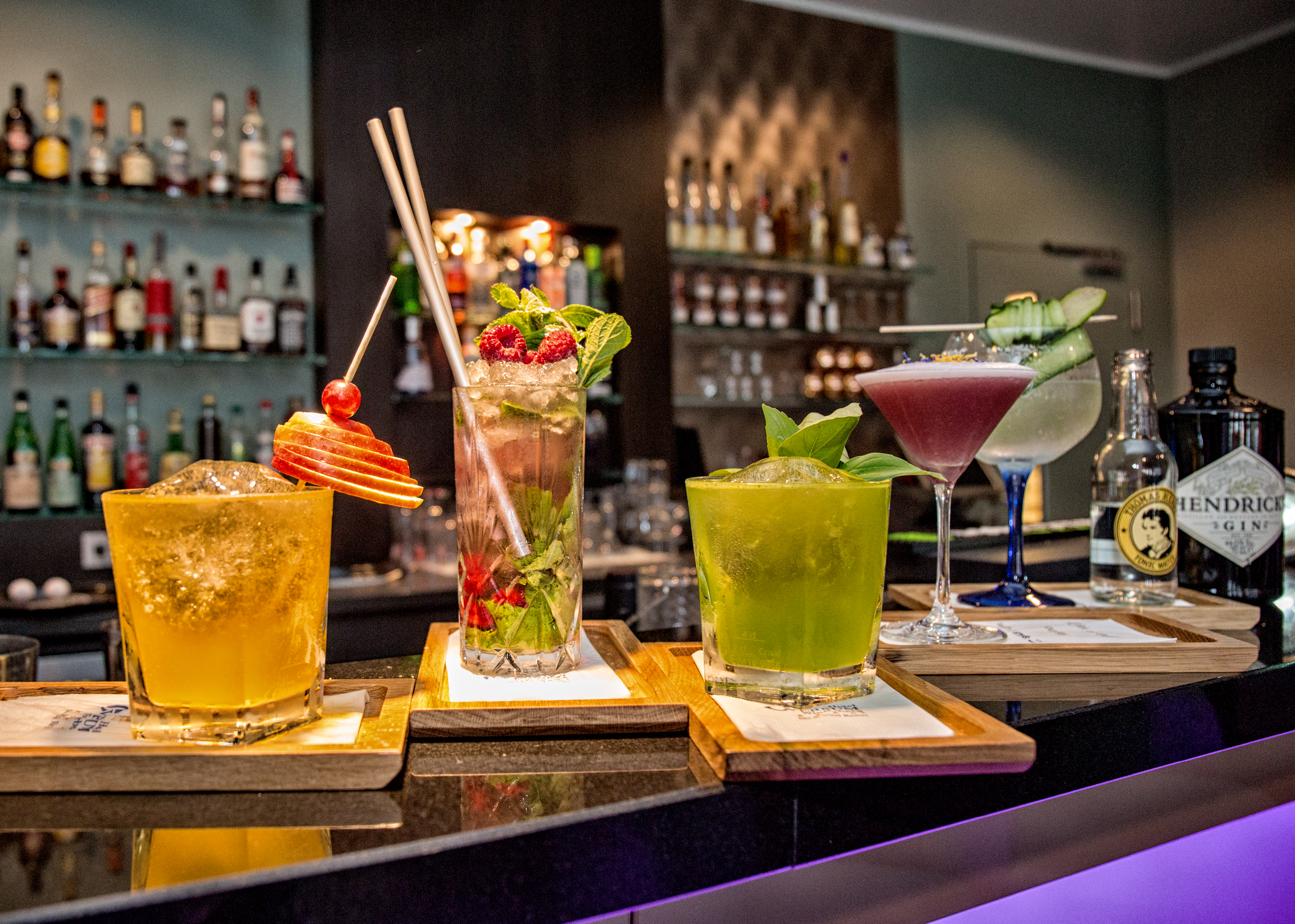 Mehrere verschiedene mit Früchten dekorierte Cocktails auf einem Tresen mit der Bar im Hintergrund. Mehrere verschiedene mit Früchten dekorierte Cocktails auf einem Tresen mit der Bar im Hintergrund.