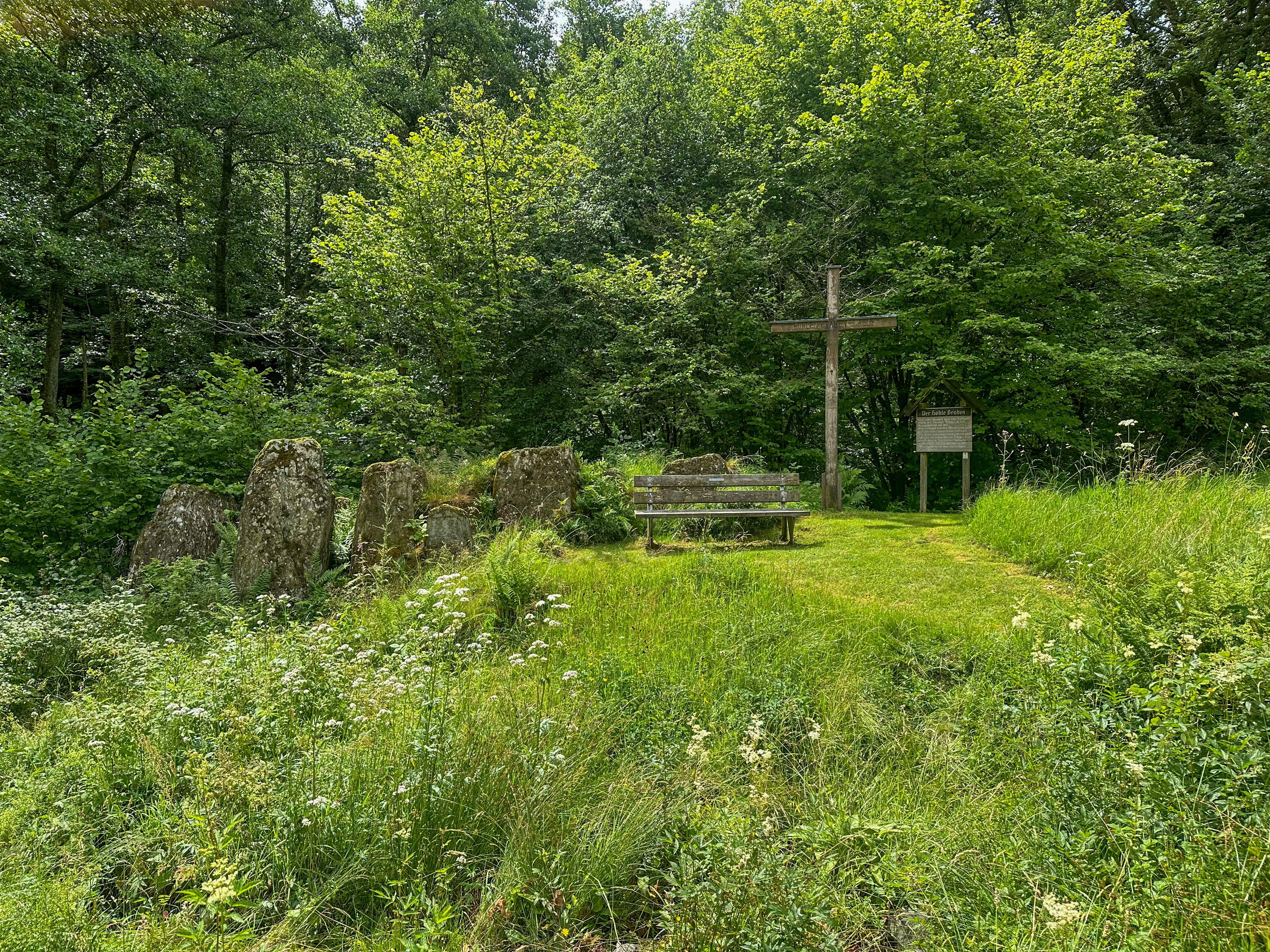 Eine Ansammlung von großen Steinen neben einer Bank und einem großen Holzkreuz, sowie einer alten hölzernen Tafel mit Informationen zu den Opfersteinen im Hohlen Graben. Eine Ansammlung von großen Steinen neben einer Bank und einem großen Holzkreuz, sowie einer alten hölzernen Tafel mit Informationen zu den Opfersteinen im Hohlen Graben.