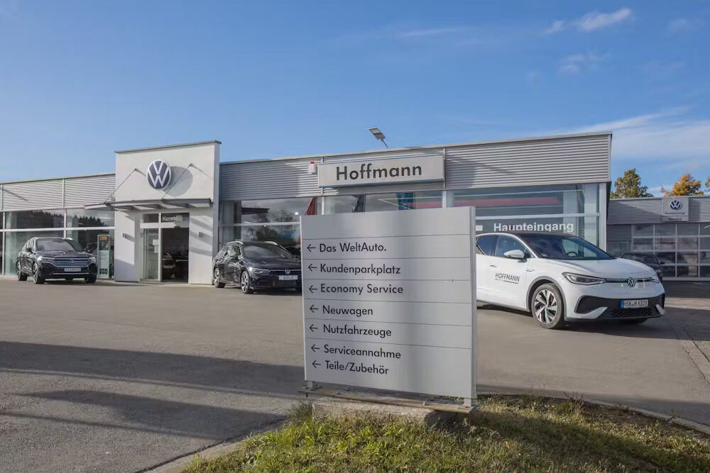Außenaufnahme des Autohauses Hoffmann mit einer Informationstafel im Vordergrund.