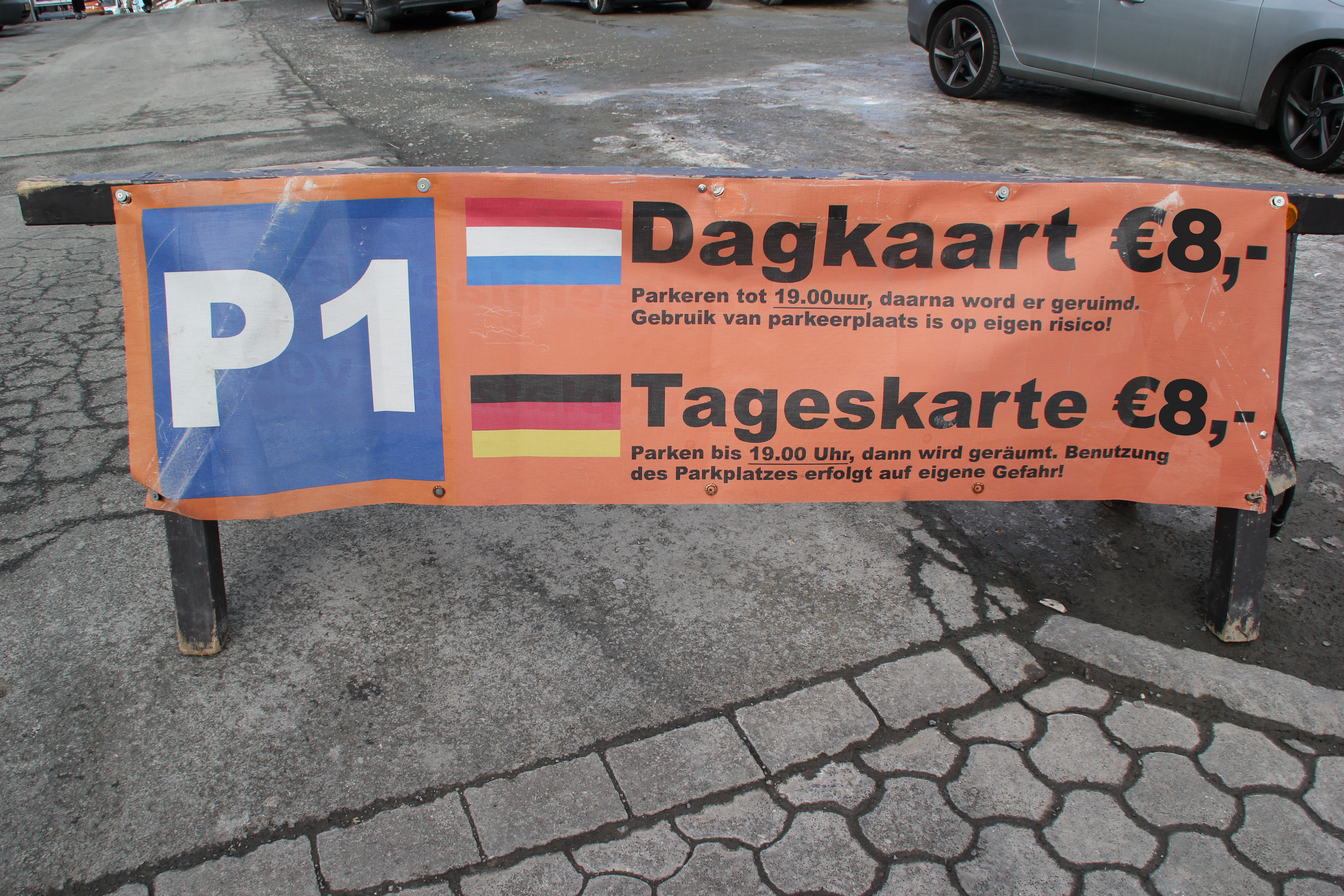 Plakat mit einem Parkplatzschild mit der Aufschrift P1 und den niederländischen und deutschen Angaben zu den Kosten einer Tageskarte.